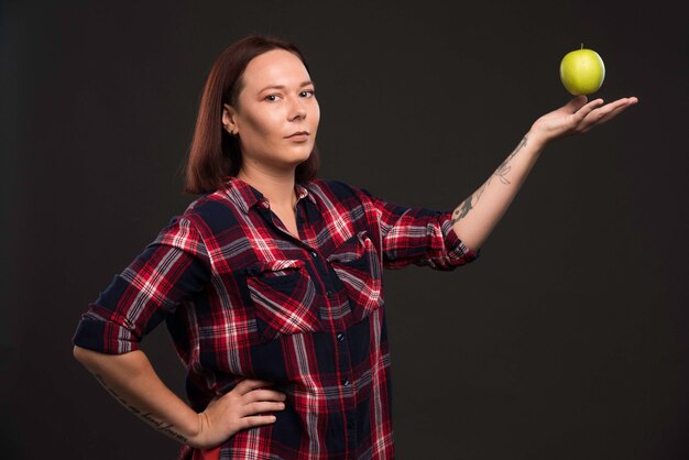 Modelo femenino en trajes de colección otoño invierno sosteniendo una manzana verde en la mano abierta.