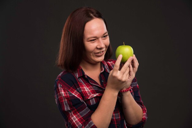 Modelo femenino en trajes de colección otoño invierno sosteniendo una manzana verde y mirando con apetito.