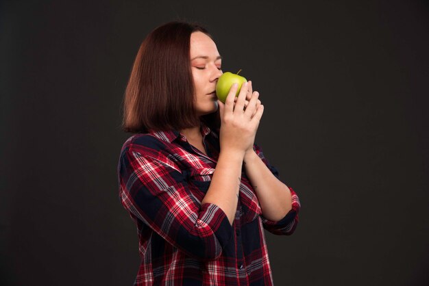 Modelo femenino en trajes de colección otoño invierno sosteniendo una manzana verde y oliéndola.