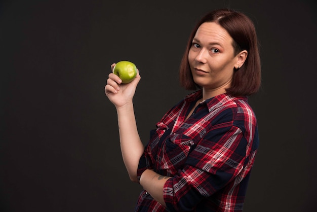 Modelo femenino en trajes de colección otoño invierno sosteniendo una manzana verde.