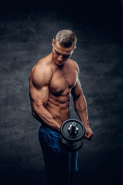 Modelo de fitness masculino joven sin camisa atlético sostiene la pesa con luz aislada sobre fondo oscuro.