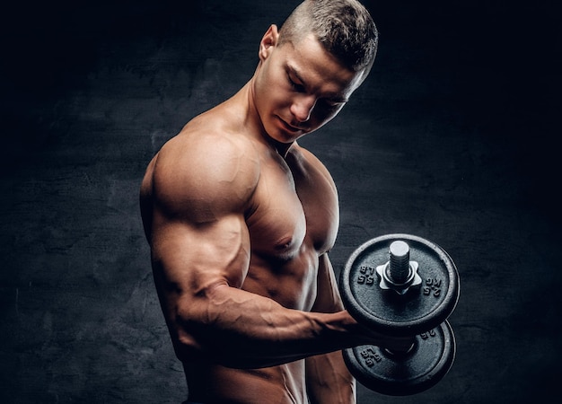 Modelo de fitness masculino joven sin camisa atlético sostiene la pesa con luz aislada sobre fondo oscuro.