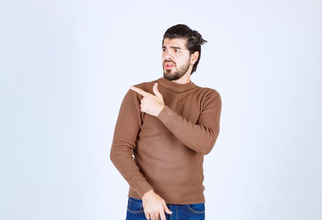 Un modelo de hombre joven con barba de pie y apuntando hacia afuera con el dedo índice. Foto de alta calidad