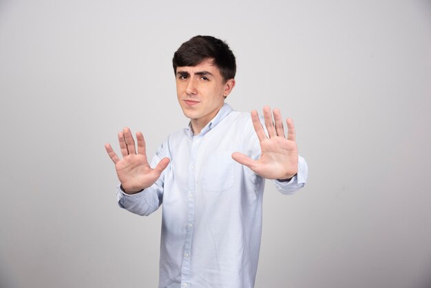 Un modelo de hombre joven en camiseta blanca de pie y mostrando la señal de stop