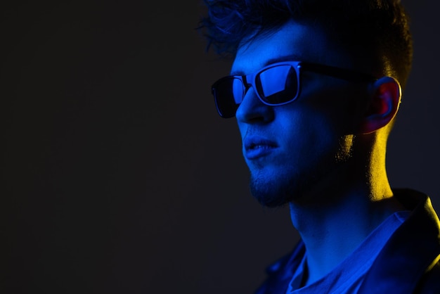 Modelo de hombre joven con sonrisa en chaqueta de cuero negra de moda en coloridas luces de neón rosa