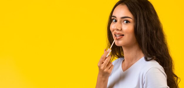 Modelo joven aplicando brillo de labios y sonriendo