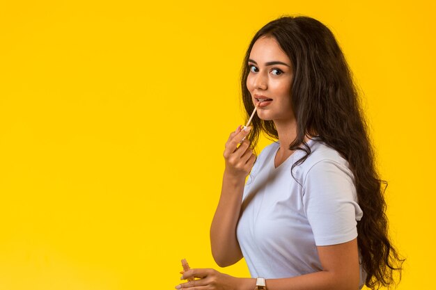 Modelo joven aplicando brillo de labios y sonriendo.