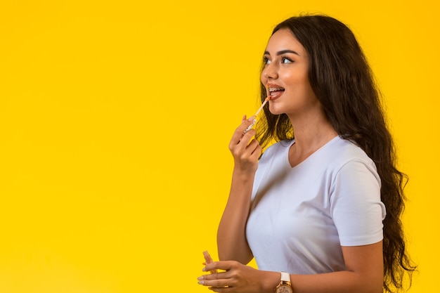 Modelo joven aplicando brillo de labios y sonriendo.