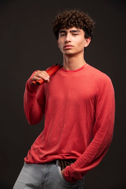 Modelo joven en camisa roja con nunchaku de karate.