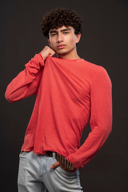 Modelo joven en camisa roja posando poniendo las manos en su cuello.