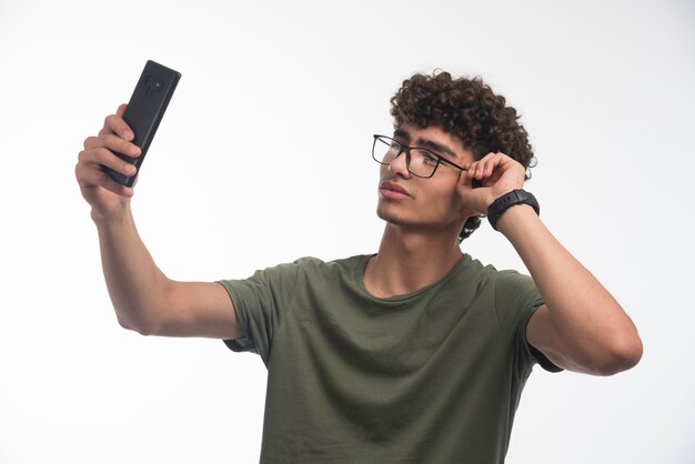 Modelo joven con pelos rizados tomando su foto y usando anteojos.