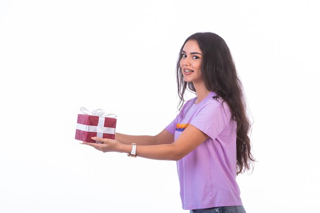 Modelo joven sosteniendo una caja de regalo roja, vista de perfil.