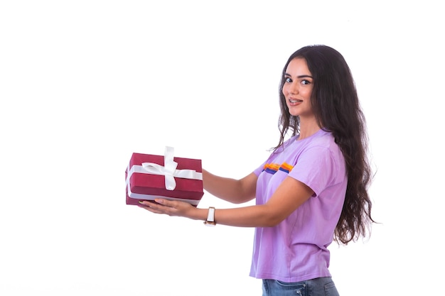 Modelo joven sosteniendo una caja de regalo roja, vista de perfil.