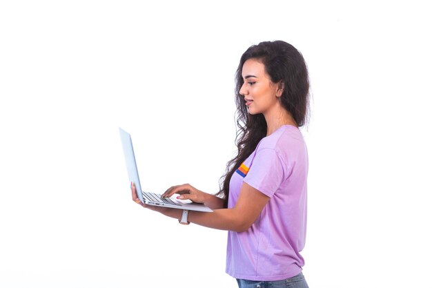 Modelo joven sosteniendo una computadora portátil plateada y con videollamada, vista de perfil.