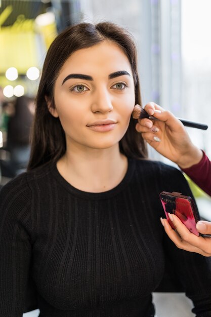 Modelo joven en suéter negro tiene procedimiento de maquillaje