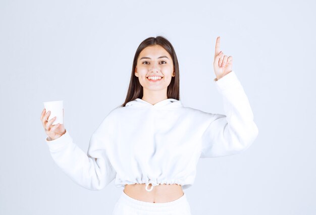 modelo linda chica joven con un vaso de plástico apuntando hacia arriba.