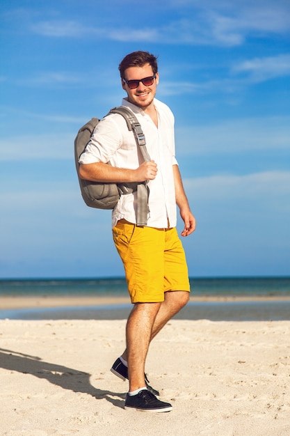 Modelo masculino joven disfrutando de las vacaciones de verano junto al mar con mochila elegante