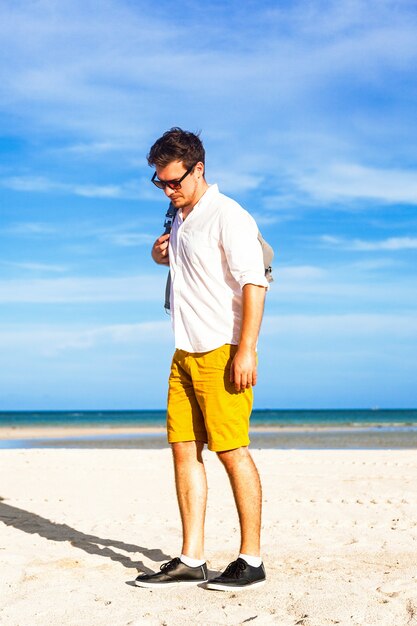 Modelo masculino joven disfrutando de las vacaciones de verano junto al mar con mochila elegante