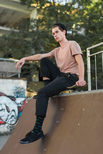 Modelo masculino joven sentado sobre la patineta