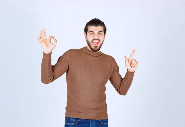 Un modelo masculino joven en suéter marrón de pie sobre una pared blanca. Foto de alta calidad
