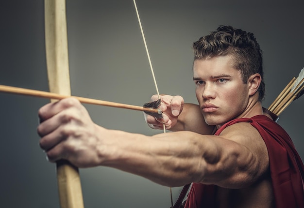 Modelo masculino musculoso con arco aislado en un fondo gris.