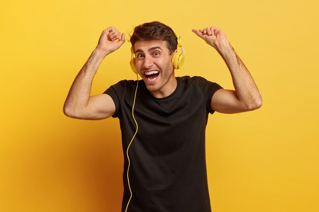 El modelo masculino relajado y despreocupado baila alegremente, escucha música en auriculares, disfruta de una buena calidad de sonido