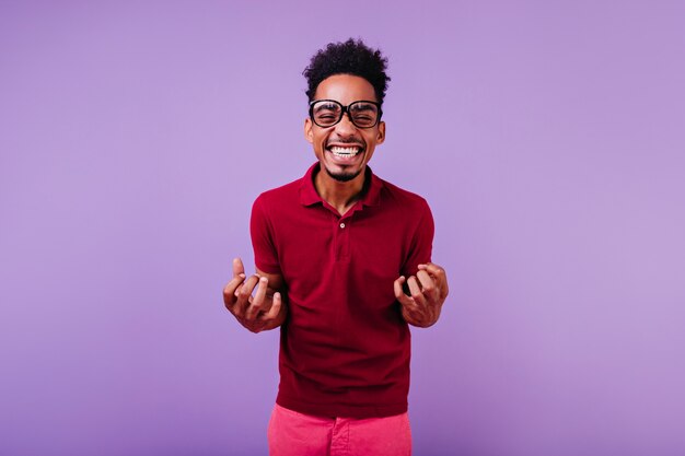 Modelo masculino rizado de pelo corto riendo. Chico africano inspirado en gafas posando.