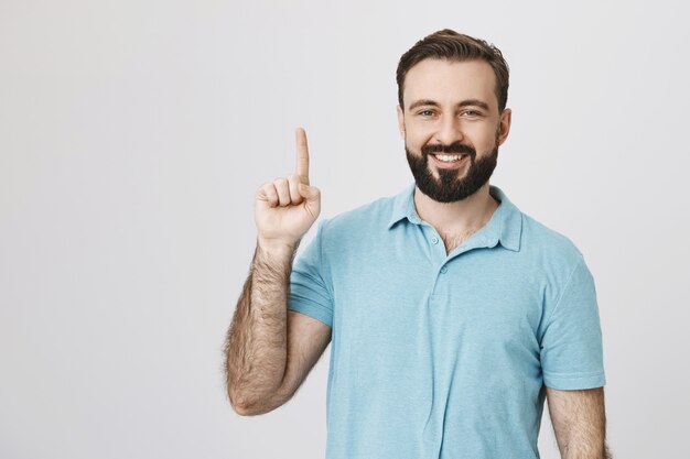 Modelo masculino satisfecho sonriendo, apuntando hacia arriba