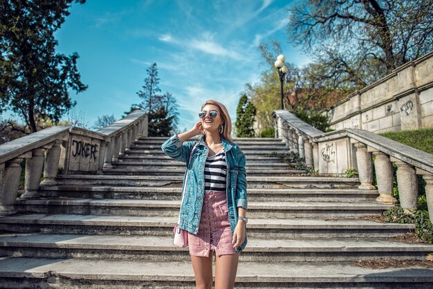 Modelo de moda hermosa posando en las escaleras llevaba falda rosada, rayas y chaqueta de mezclilla