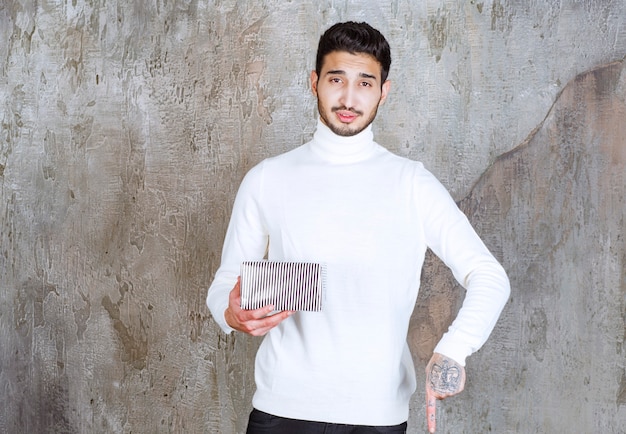 Modelo de moda en suéter blanco sosteniendo una caja de regalo plateada y llamando o invitando a alguien a su lado.