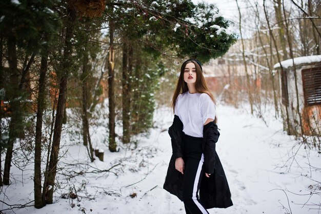 Modelo morena de piernas largas de moda en capa negra larga y sombrero al aire libre en el día de invierno