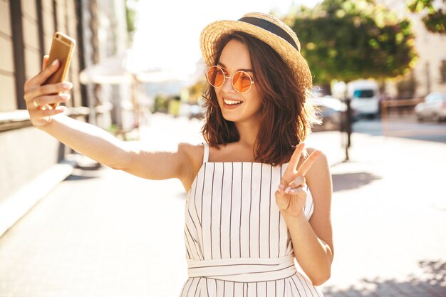 modelo morena en ropa de verano posando en la calle mediante teléfono móvil