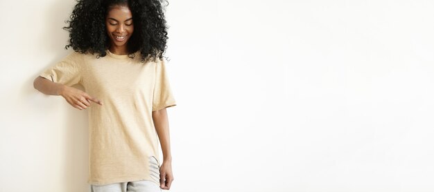 Modelo de mujer africana joven atractiva con camiseta casual, sonriendo y mostrando su camiseta en blanco