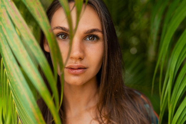 Modelo de mujer agraciada de cerca en traje de baño rojo con pelo largo y recto posando en la naturaleza tropical.