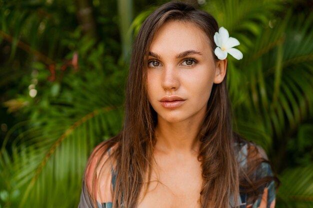 Modelo de mujer agraciada cercana con flor de plumeria en los pelos posando en la naturaleza tropical