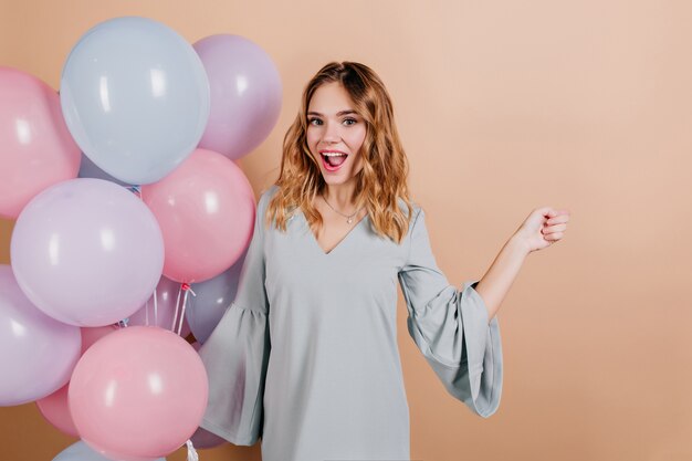 Modelo de mujer bastante europea en traje azul posando con sonrisa de sorpresa al lado de globos