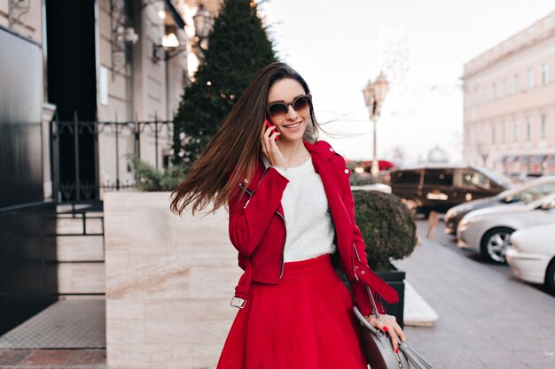 Modelo de mujer blanca joven complacida en traje rojo hablando por teléfono