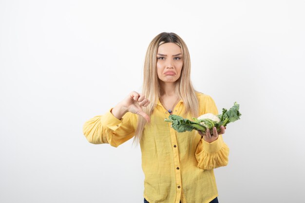 modelo de mujer bonita con coliflor mostrando un pulgar hacia abajo.