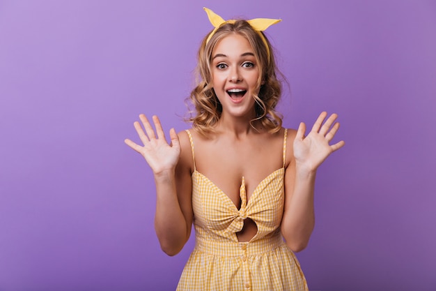 Modelo de mujer bronceada alegre con cinta amarilla riendo. Retrato de niña increíble con cabello rubio ondulado.