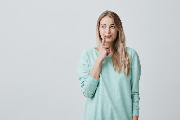 Modelo de mujer caucásica con largo cabello rubio vestido casualmente mira a un lado con expresión soñadora