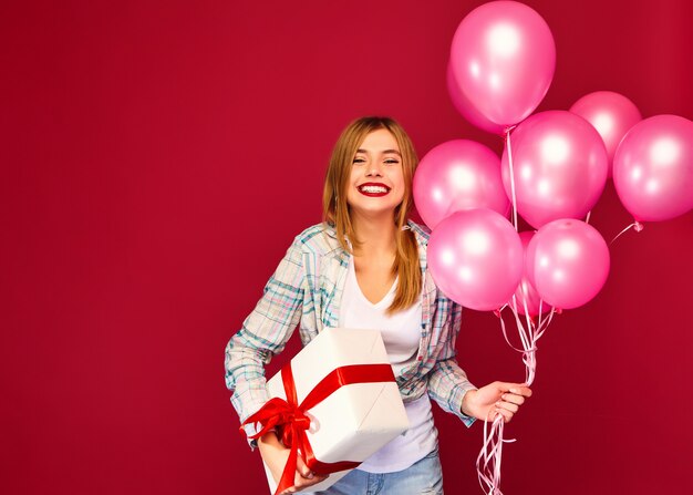 Modelo de mujer celebrando y sosteniendo caja con regalo presente y globos rosados