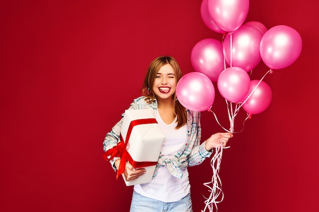 Modelo de mujer celebrando y sosteniendo caja con regalo presente y globos rosados