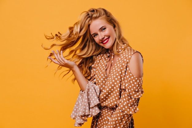 Modelo de mujer entusiasta con peinado elegante sonriendo. Foto interior de adorable joven posando con placer en la pared amarilla.