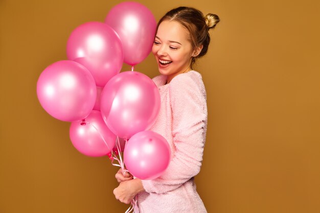 Modelo de mujer con globos rosados en la pared dorada