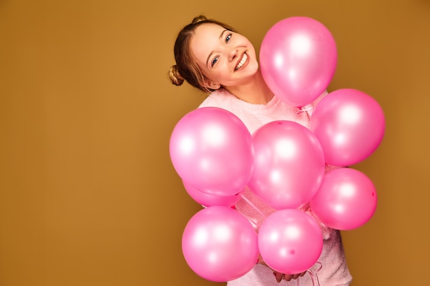 Modelo de mujer con globos rosados en la pared dorada