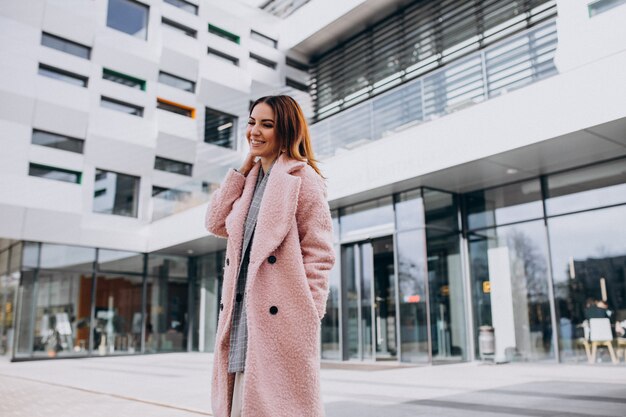 Modelo de mujer joven en abrigo rosa por el edificio