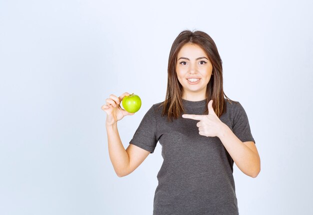 modelo de mujer joven apuntando a una manzana verde.