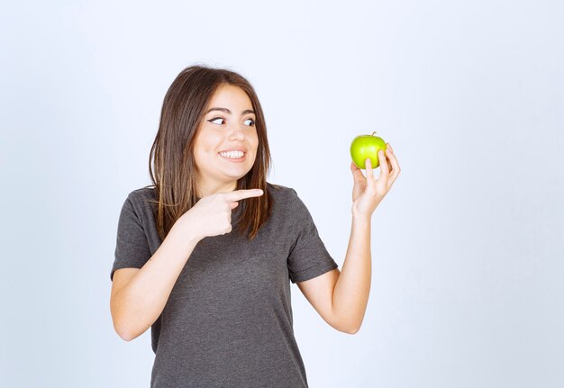 modelo de mujer joven apuntando a una manzana verde.