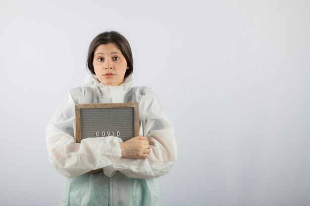 modelo de mujer joven en bata de laboratorio defensiva de pie sobre una pared blanca.