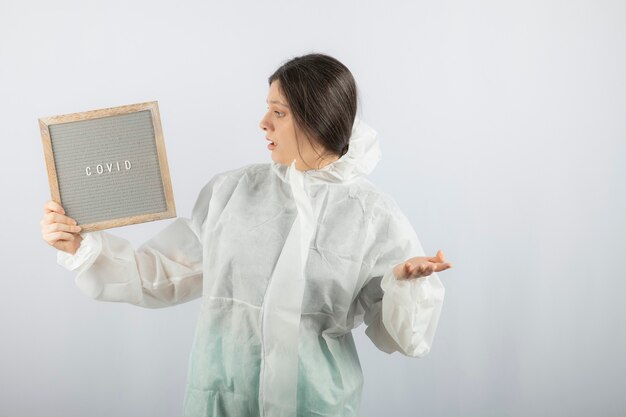 modelo de mujer joven en bata de laboratorio defensiva de pie sobre una pared blanca.